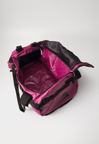 Pink duffel bag featuring a glossy interior, black straps, and a mesh top section. It has a durable exterior with a logo on the side.