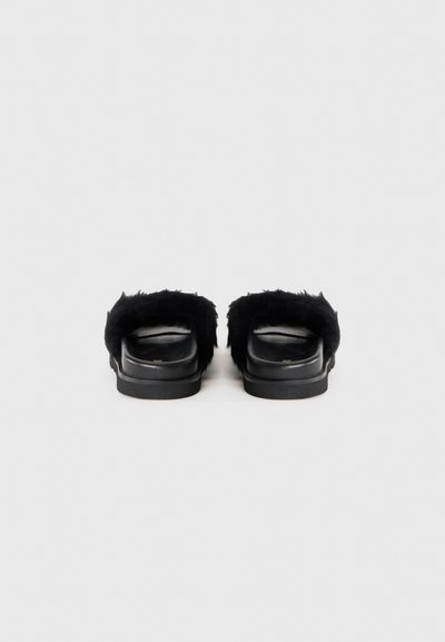 Sandale negre cu un brâu texturat pufos și talpă netedă neagră; design plat, minimalist, fără hardware vizibil.