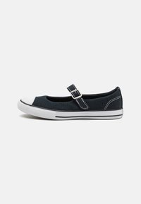 Zapato plano tipo Mary Jane de lona negra con punta blanca, correa ajustable con hebilla, franjas laterales blancas y suela de goma.