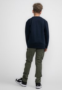 Marineblauwe sweatshirt met lange mouwen en een ronde hals, gecombineerd met olijfgroene cargobroeken met zijzakken. Zwart-witte sneakers.