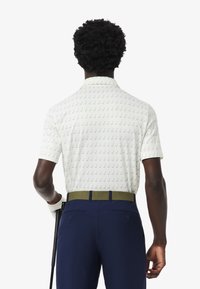 Polo shirt bianco a maniche corte con motivo a golf club verde, abbinato a pantaloni blu navy e una cintura a coste verde oliva. Design del tessuto texture.