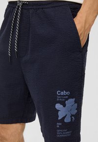 Shorts bleu marine en tissu texturé, avec une taille élastique munie d'un cordon de serrage, des poches latérales et un détail logo floral imprimé.