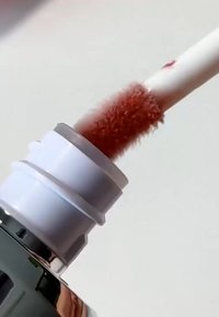Bâtonnet de gloss à lèvres avec une brillance rose-brun tiré d'un tube argenté brillant et blanc sur un fond clair.