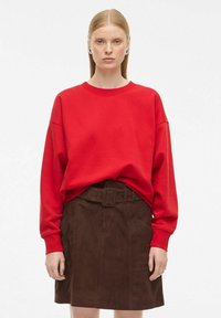 Röd sweatshirt med långa ärmar och rund halsringning, kombinerad med en brun mockaskirt med bälte och sidofickor.