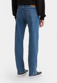 Pantalones vaqueros azules de mezclilla con un diseño de pierna recta, que cuentan con bolsillos traseros y una etiqueta de cuero en la cintura. Combinados con zapatillas verdes y blancas.