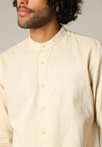 Crèmekleurig, knoopshirt met een bandkraag, gemaakt van lichte stof, met een gladde textuur en subtiele glans.