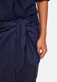 Mørkeblå lin kjole med frontbånddetalj, med en glatt tekstur og løs passform, fremhevet av et stilrent, minimalistisk design.