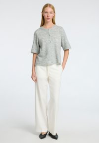 Maglione grigio chiaro a maniche corte e bottoni realizzato in materiale morbido, abbinato a pantaloni bianchi a gamba larga e mocassini neri.