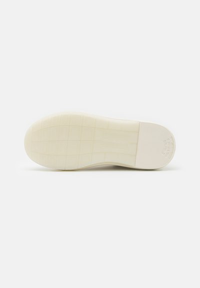 Zadnji del športnih copat je v enotni beli barvi, strukturiran z majhnimi kvadratnimi vzorci in logotipom na peti. Gladka, zaobljena zasnova.