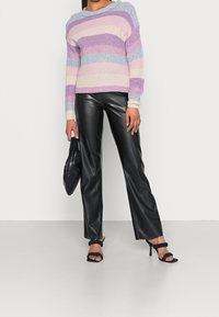 Pull tricoté à rayures horizontales multicolores en violet, rose et bleu. Associé à un pantalon slim en cuir noir et des talons noirs à brides.