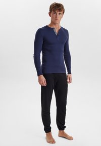 Mørkeblå langærmet henley skjorte med knaplukning, parret med sorte tapered sweatpants med elastiske manchetter. Stof ser blødt ud.