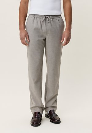 Man wearing light gray checkered drawstring pants and dark brown leather loafers, standing against a plain light background.