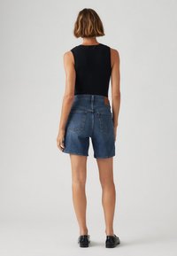 Denimshorts med medelhög midja, mörk tvätt och klassisk femficksdesign. Ribbade svarta ärmlösa toppar, enkla mörka skor.