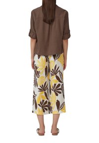 Bruine kortek mouwen shirt gecombineerd met brede pantalons met een patroon van gele en bruine bladeren. Sandalen met een strikdetail.