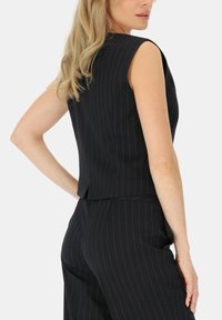 Czarny bezrękawnik w paski z wysokim dekoltem i dopasowanym krojem, z prostym dołem i gładką teksturą. Skordynowany z dopasowanymi spodniami.