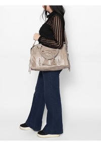 Sac à main en cuir gris avec poignée tressée, grand compartiment principal, ferrures décoratives et accents de pompons. Design minimaliste, texture douce.