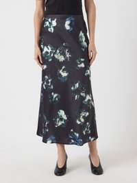 Ženska v črni satenski midi krilu z abstraktnimi modrimi in belimi cvetličnimi vzorci, v kombinaciji s črnimi petkami in črnim zgornjim delom.