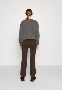 Sweatshirt gris à coupe décontractée avec des poignets côtelés, associé à un pantalon ajusté marron foncé, tous deux en tissu doux. Des chaussures noires complètent le look.