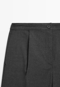 Pantaloni grigi su misura con una texture liscia, dotati di pieghe frontali, chiusura con un solo bottone e tasche infilate sui lati.