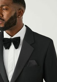 Sort smokingjakke med spidse revers, hvid plisseret skjorte og sort fløjl butterfly. Lommetørklæde i matchende stof.