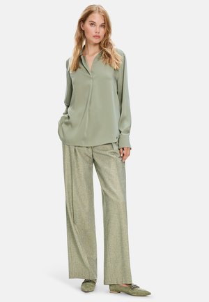 Hellgrüne Bluse mit Kragen und langen Ärmeln, kombiniert mit weit geschnittenen, gemusterten Hosen in einem passenden Farbton. Einfache grüne Ballerinas.