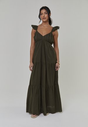 Robe longue vert foncé, avec des bretelles à volants, un profond décolleté en V et une jupe à volants. Fabriquée en tissu léger à la texture lisse.