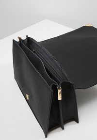 Sac en cuir noir au design structuré. Comprend des accessoires en métal doré, plusieurs compartiments et une section zippée pour l'organisation.