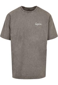 Camiseta de algodón de manga corta gris con cuello redondo y la palabra "Inspire." impresa en blanco en el lado izquierdo. Textura suave y ligeramente desgastada.