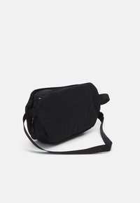 Bolso de hombro negro fabricado en un tejido suave, con forma rectangular, diseño acolchado y una larga correa ajustable con cierre de cremallera.
