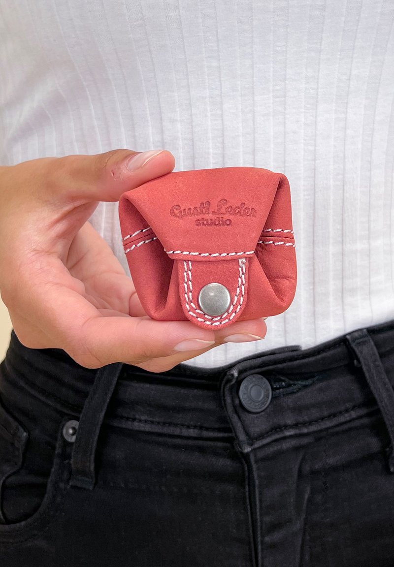 Červená kožená taška s bílým prošitím a zavíráním na patent, s ražbou "Gastil Leder studio," držena v ruce. Kompaktní a hladká textura.