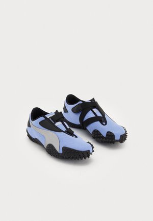Scarpe da ginnastica azzurro chiaro con tomaia in tela testurizzata, dettagli neri e suola in gomma robusta con punte pronunciate per una maggiore aderenza.