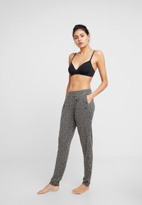 Schwarz-weiße gemusterte Hose mit lockerem Sitz, seitlichen Taschen und schmal zulaufendem Bein. Das Model trägt ein schwarzes Bralette.