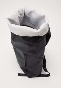 Zwarte rugzak met een opgerolde bovenkant, polyester buitenkant, gestreepte katoen lining, ritszak en verstelbare schouderbanden. Gestructureerde afwerking.