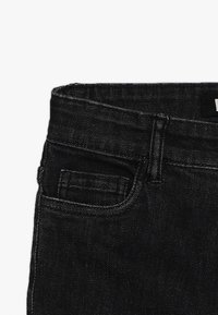 Pás a horní část černých džín s přední kapsou a viditelným poutkem na opasek na čistém bílém pozadí.