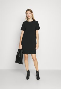 Black short-sleeve dress with a round neckline, slim fit, above-knee length, paired with a black leather bag and ankle boots. Smooth texture.