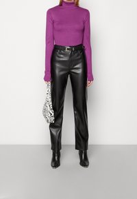 Personne portant un col roulé violet, un pantalon en cuir noir avec ceinture, des bottes pointues noires, et tenant un sac à main imprimé zèbre noir et blanc.