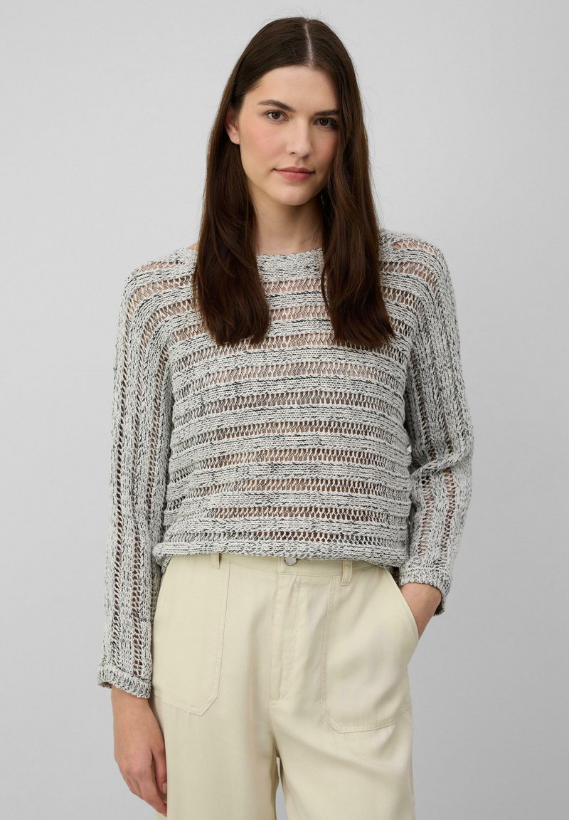 Hellgrauer gestrickter Pullover mit breiten, horizontalen Streifen und lockerer Passform. Lange Ärmel mit gerippten Bündchen. Kombiniert mit cremefarbenen Hosen.