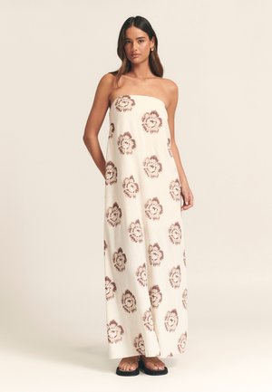 Maxi dress in cream fabric with brown floral patterns, strapless design, relaxed fit, and floor-length. Worn with black flat sandals.