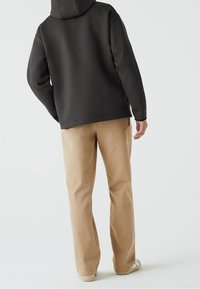 Sweat à capuche gris foncé et pantalon beige clair. Le sweat a une coupe décontractée et le pantalon est droit avec une texture lisse.