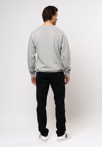 Grijze sweatshirt met een ronde halslijn en lange mouwen, gecombineerd met zwarte broek en witte sneakers. De sweatshirt heeft een gladde textuur.