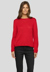 Roter, strukturierter Pullover mit Rundhalsausschnitt und langen Ärmeln, getragen mit schwarzen Hosen. Das Design zeichnet sich durch eine lockere Passform und leichte Rippungen aus.