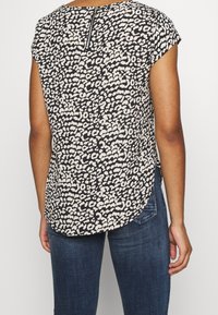 Blouse à manches courtes avec un motif imprimé léopard en noir et crème, présentant un ourlet arrondi et un zip dans le dos.