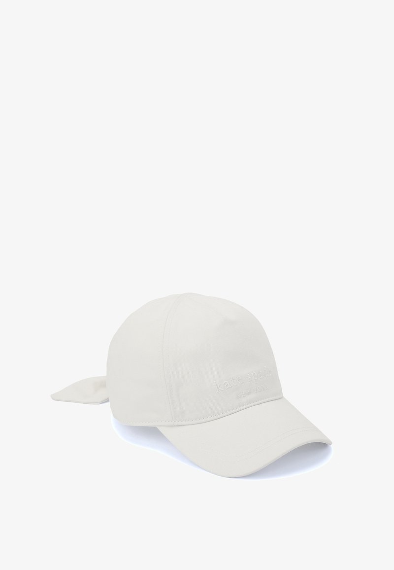 Ljusbeige keps med en böjd skärm, tygband bak och präglat varumärkesnamn "kate spade NEW YORK" på framsidan.