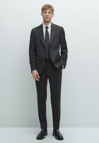 Dark gray pinstriped suit with notched lapels, paired with a white shirt and dark tie. Completed with black leather ankle boots.