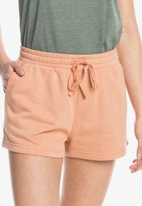 Perzikkleurige shorts van zachte stof, voorzien van een elastische tailleband met een trekkoord en zijzakken. Gladde textuur en eenvoudig ontwerp.
