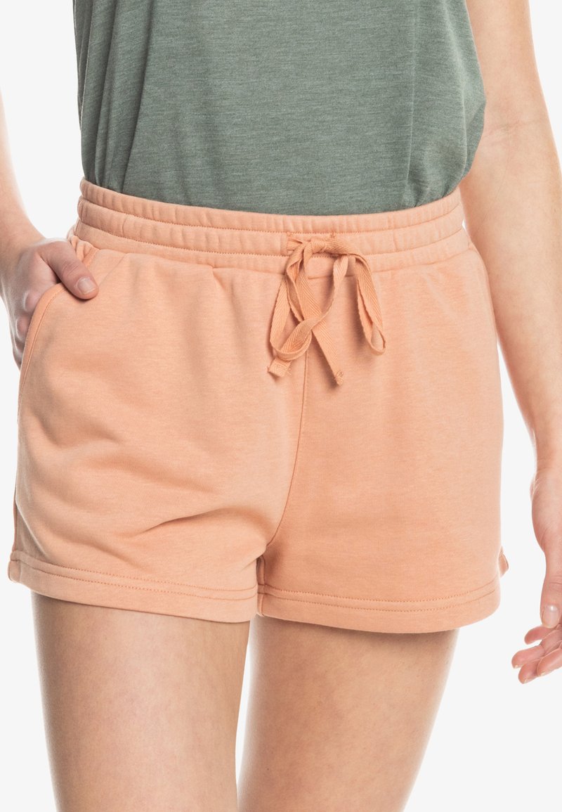 Perzikkleurige shorts van zachte stof, voorzien van een elastische tailleband met een trekkoord en zijzakken. Gladde textuur en eenvoudig ontwerp.