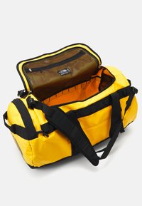 Borsa a cilindro gialla con accenti neri, forma rettangolare, materiale resistente e una tasca in rete all'interno. Dotata di spallacci regolabili e cerniere.
