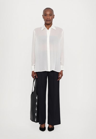 White sheer button-up shirt with a collar, paired with navy wide-leg trousers. Black tote bag and pointed black flats complete the look.