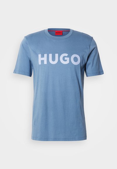 Светло синя памучна тениска с къси ръкави, с голям бял логотип "HUGO" отпред. Просто кръгло деколте, гладка текстура.