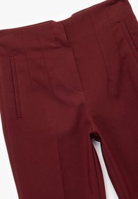 Pantalones de corte burgundy confeccionados en una tela suave, con una textura lisa, dos bolsillos delanteros y pliegues marcados en la cintura.